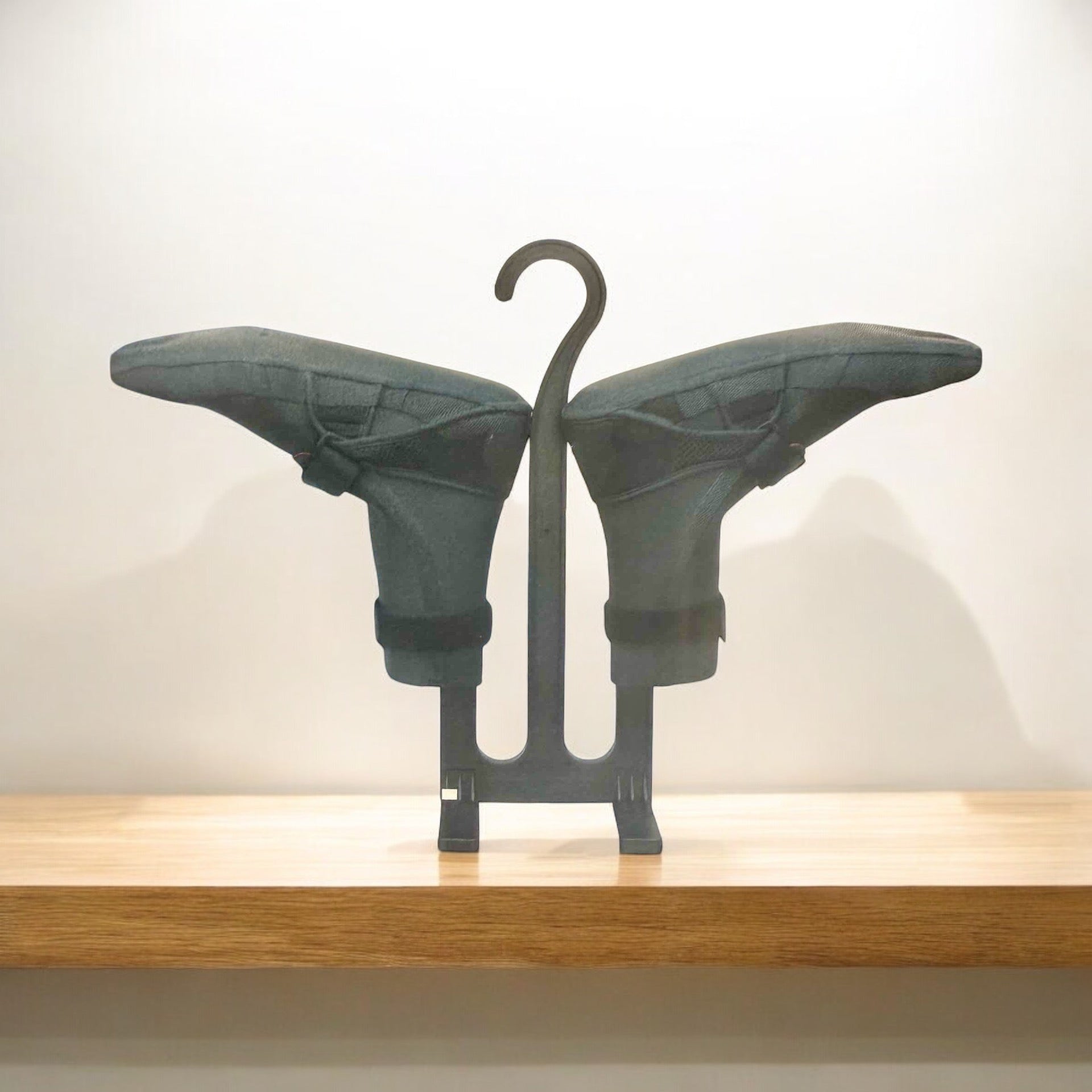 Black Block Surf wetsuit bootie drying stand with two dark grey booties on a wooden shelf.