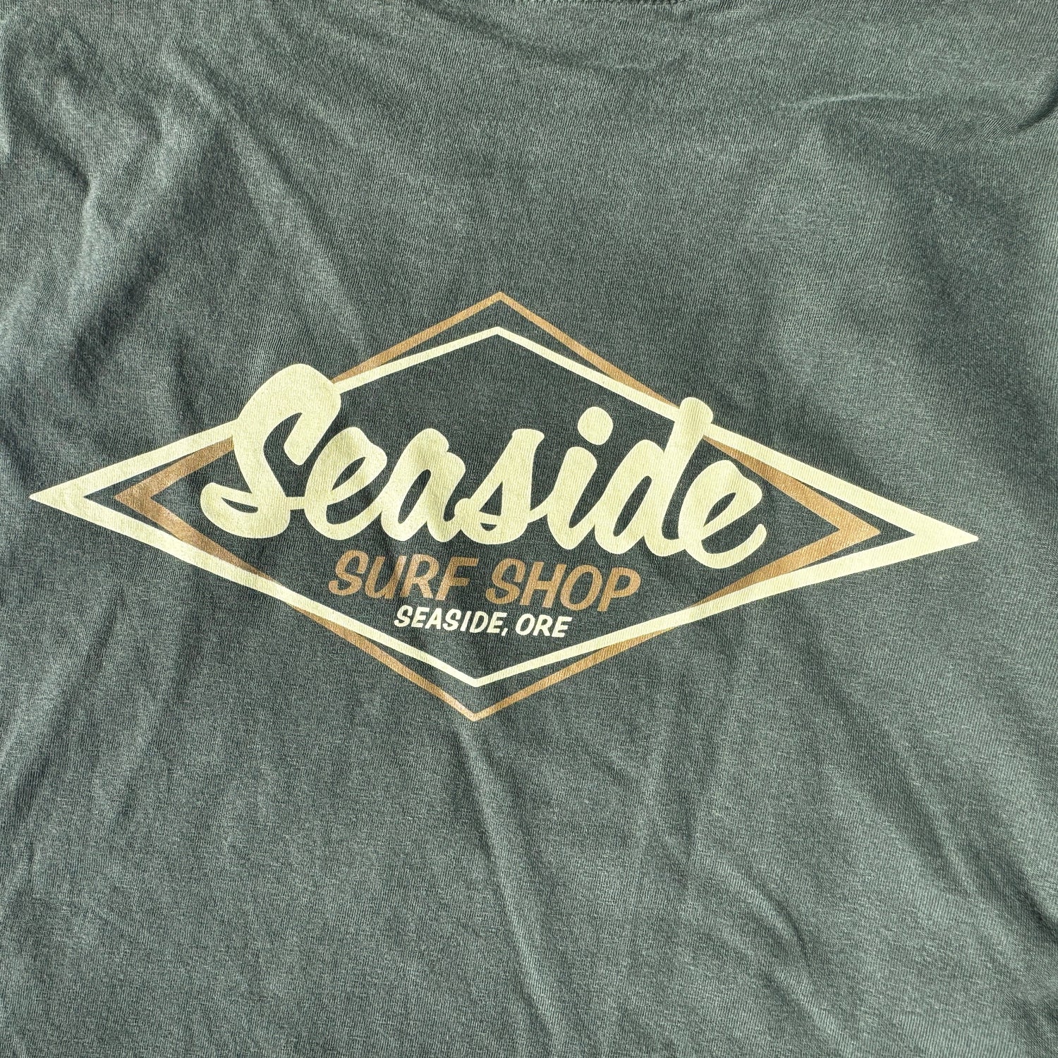 A close-up of a dark heather gray t-shirt featuring a large diamond-shaped graphic on the chest. The graphic has a cream-colored script reading &